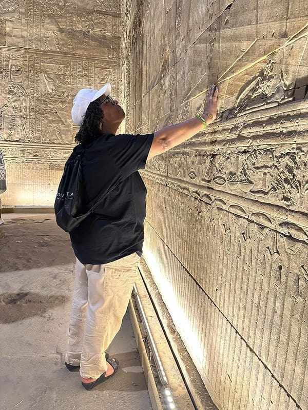 black woman experiencing the Egyptian pyramid ruins with hand on wall 