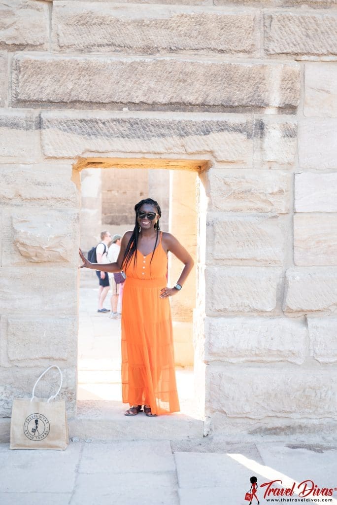 Black woman (travel diva) in the door way of a Egyptian monument with orange flowy dress.