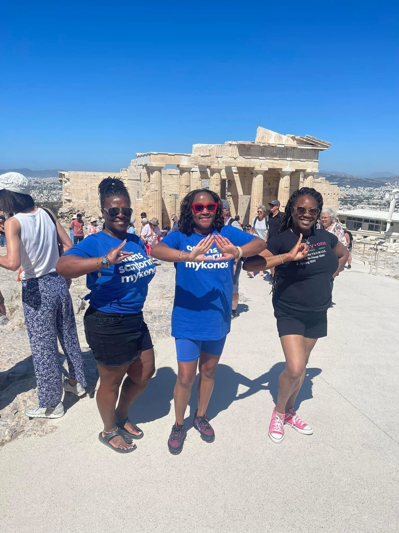 Travel Divas wearing Athens Santorini Mykonos Travel Divas tee in front of ruins in Greece.